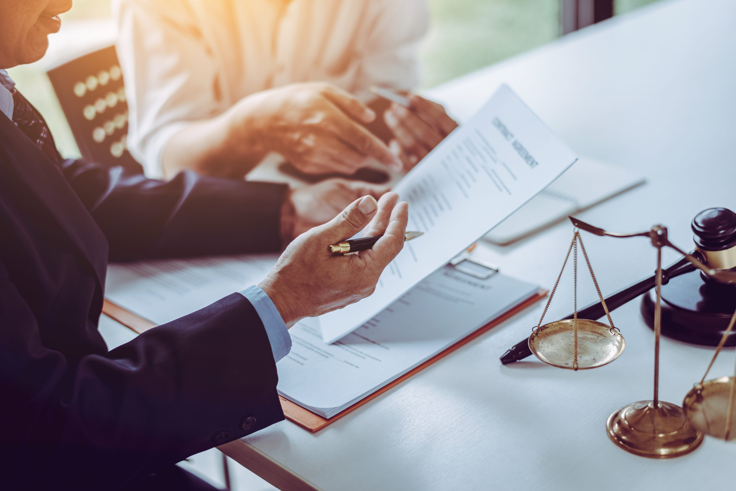 Two individuals reviewing a legal document, with a gavel and balance scale on the table, symbolizing legal consultation.