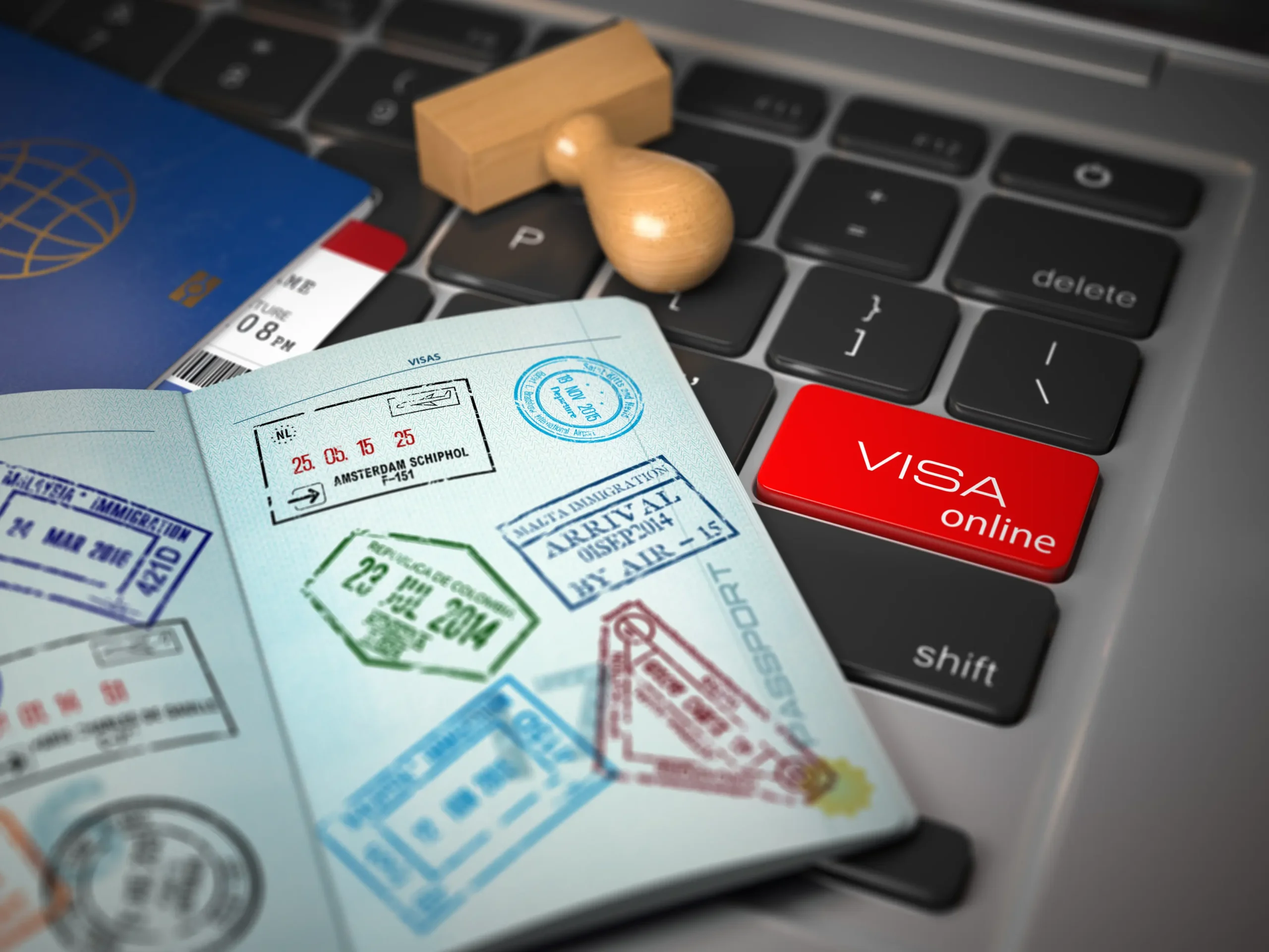 Open passport with immigration stamps, airline ticket, and a wooden stamp, on a laptop keyboard with a prominent 'VISA