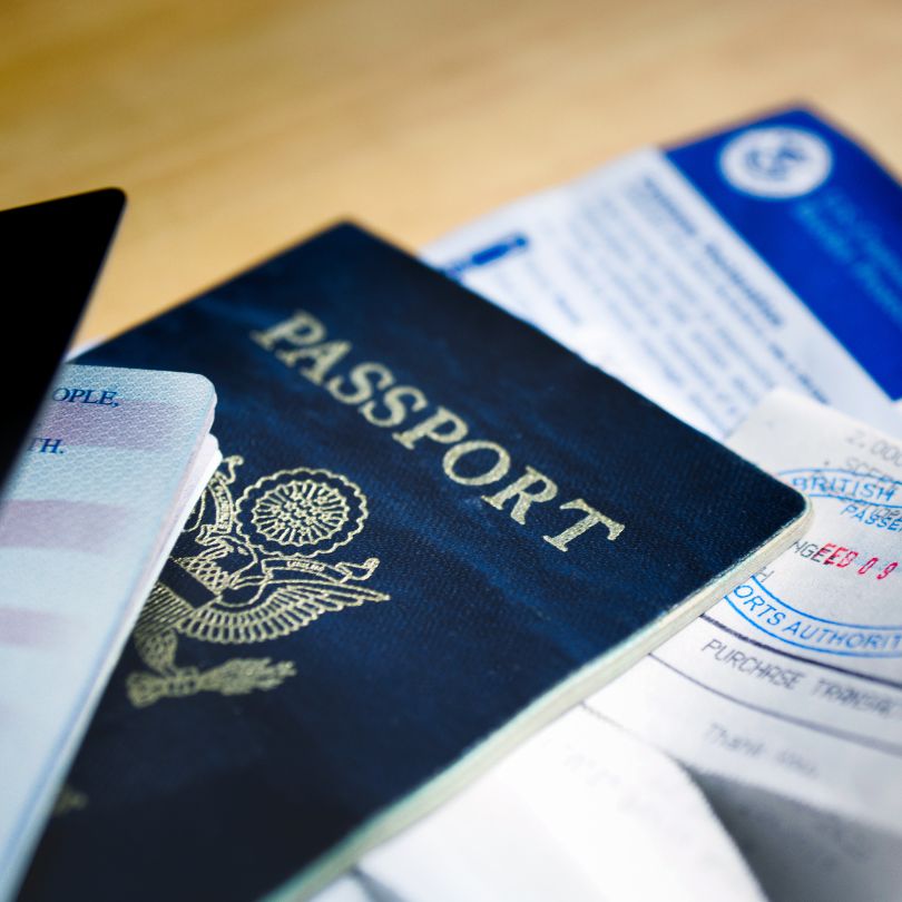 Close-up of a dark blue U.S. passport on a wooden surface, surrounded by other travel documents and papers.